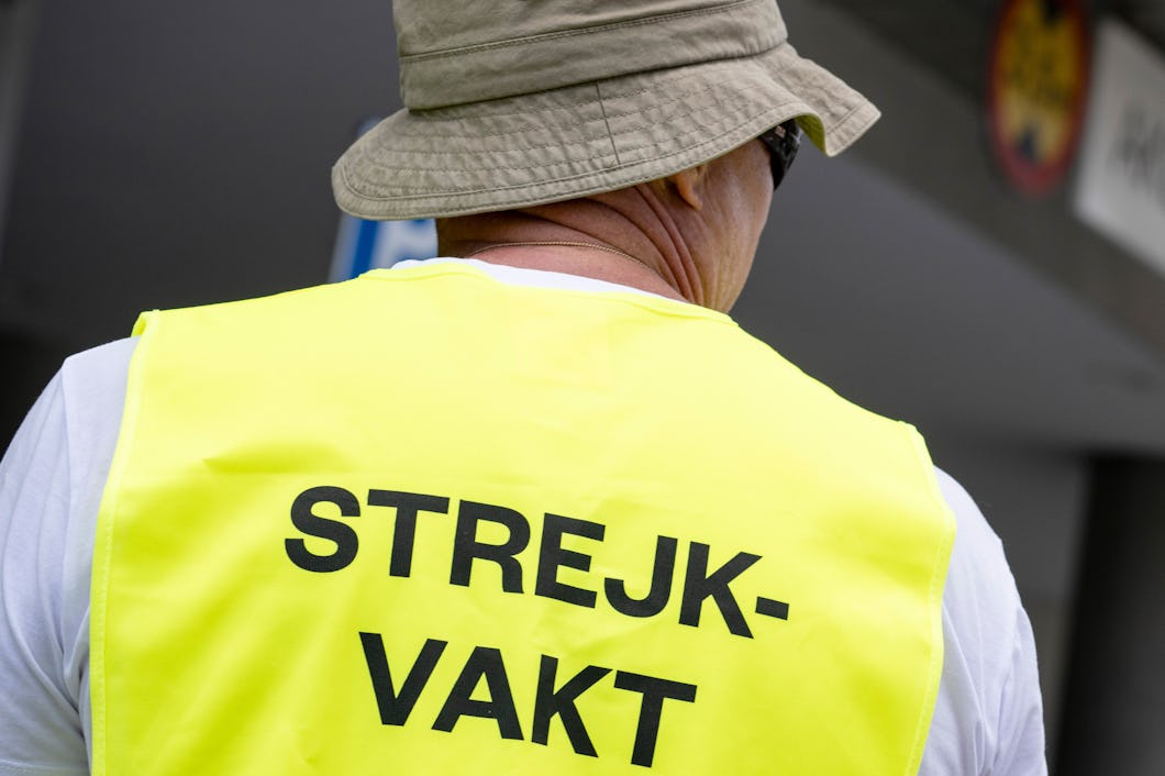 En person med en väst märkt "STREJKVAKT" står utomhus med ryggen mot kameran.