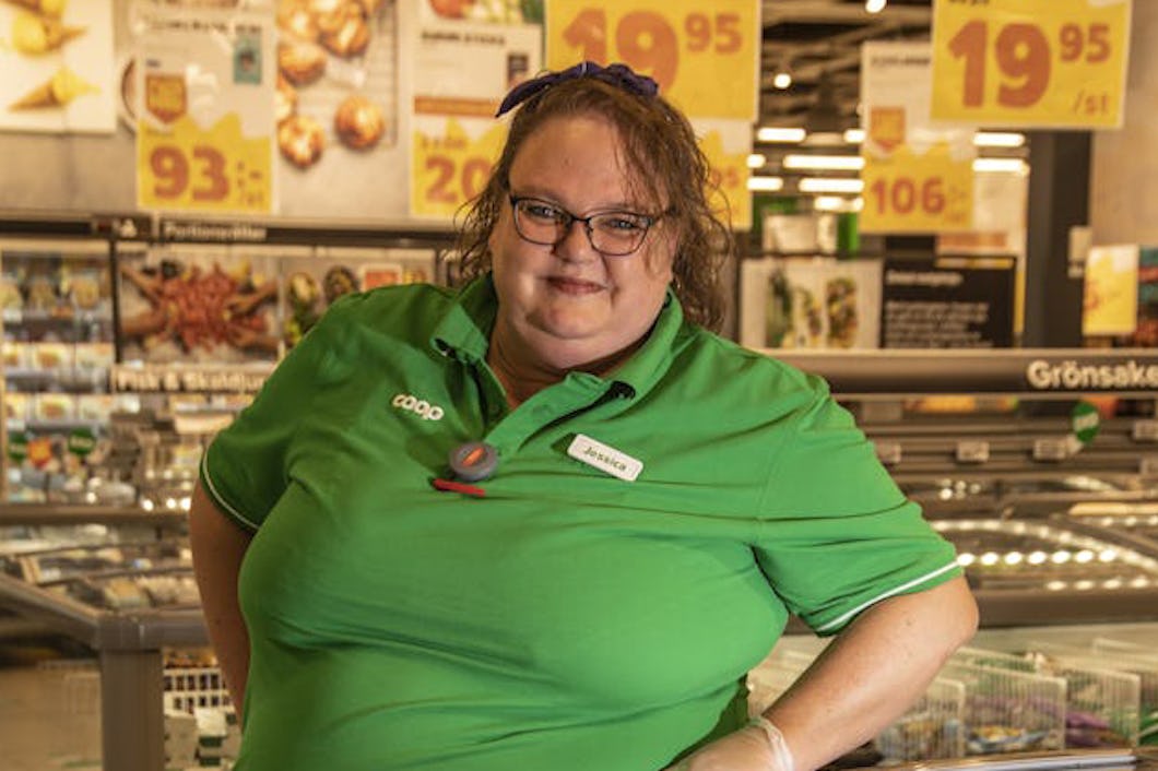 En anställd i en livsmedelsbutik, klädd i uniform, står framför frysvaror.