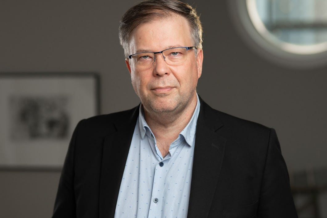 IF Metals vice ordförande Tomas With. med glasögon, skjorta och kavaj står inomhus framför en oskarp bakgrund.