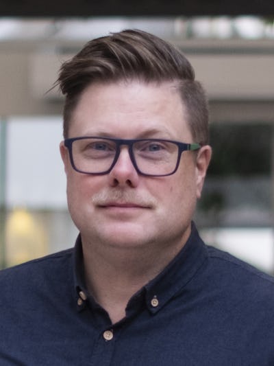 Andreas Marklund med kort hår, glasögon och mustasch står inomhus. Han har på sig en mörk skjorta och visar ingen tydligt ansiktsuttryck.