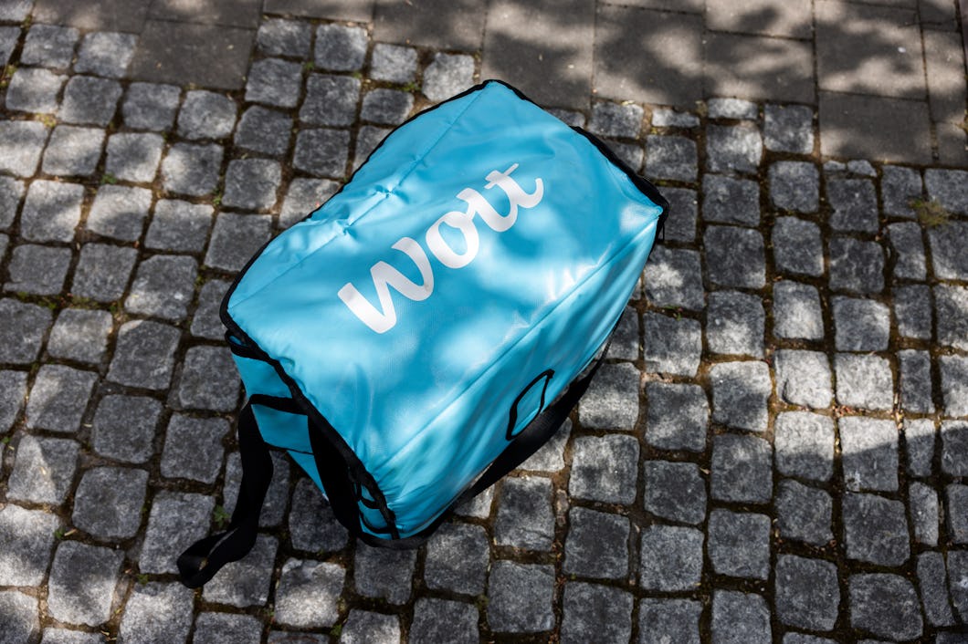 En Wolt-leveransväska står på en gatstenbelagd yta under delvis skugga.