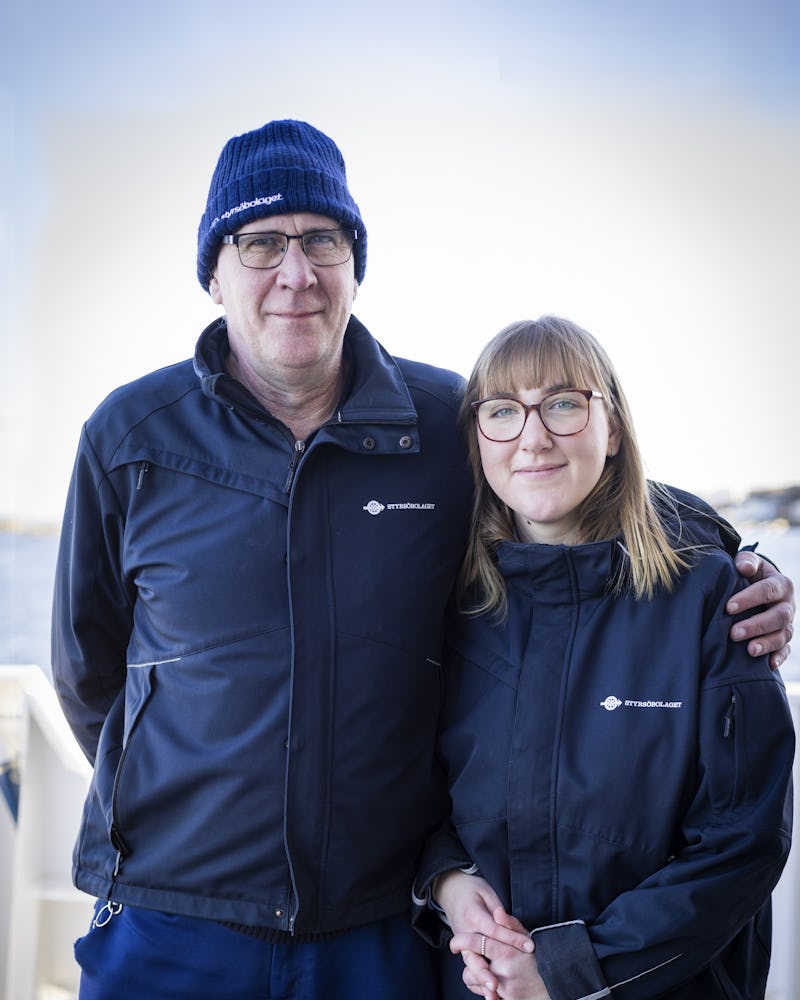 Två personer med glasögon och mörka jackor står nära varandra utomhus.
