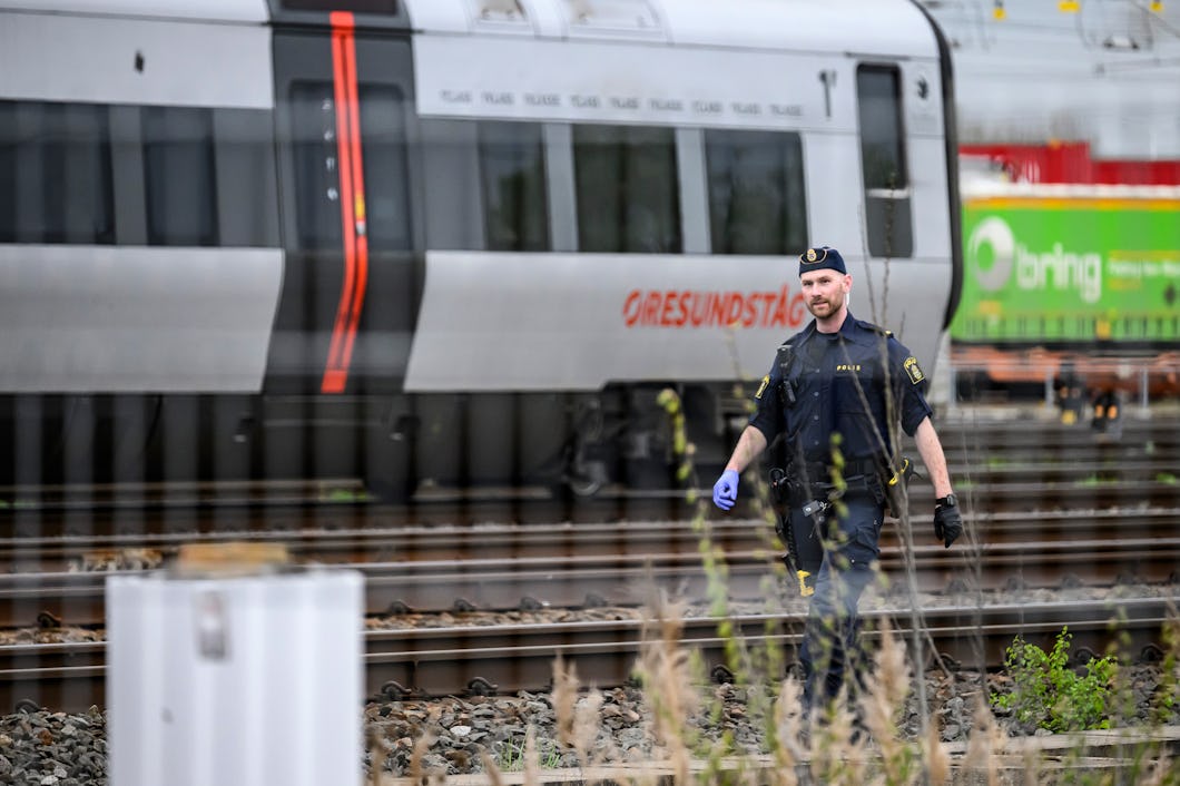 En polis går längs järnvägsspåren med ett tåg i bakgrunden.