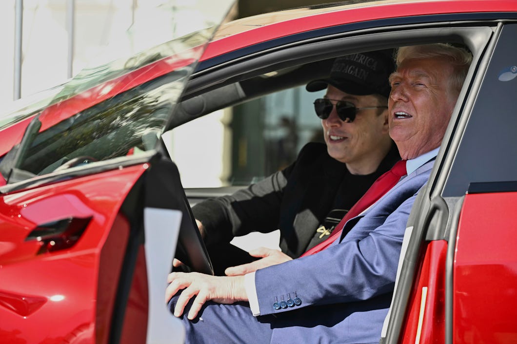 Elon Musk och Donald Trump sitter i framsätena på en röd bil med förardörren öppen; den ena har keps och solglasögon, den andra bär kostym och slips.