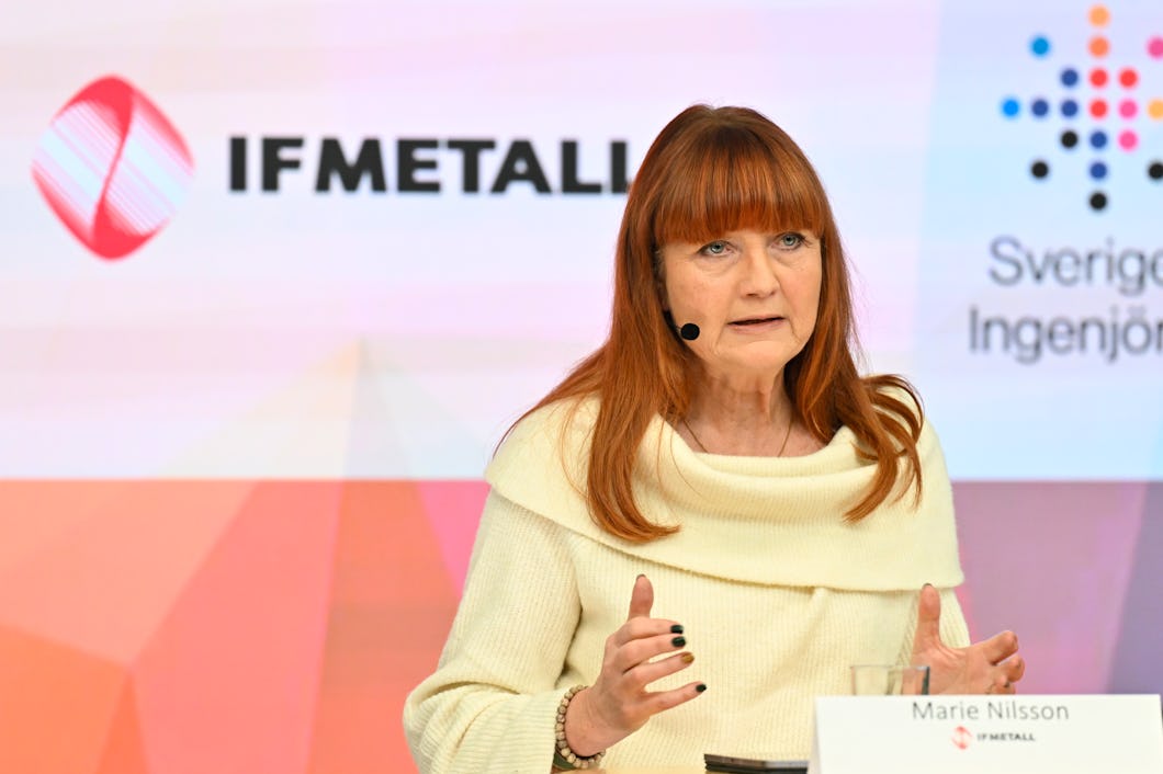 En kvinna med långt rött hår talar vid en talarstol och har ett headset med mikrofon. Bakom henne syns logotyper för IF Metall och Sveriges Ingenjörer.
