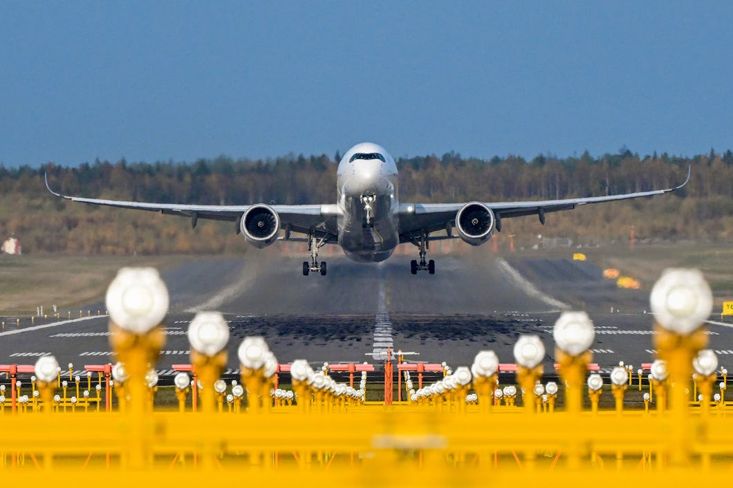 Ett passagerarflygplan lyfter från en startbana. I förgrunden finns flygplatsens landningsljus och i bakgrunden syns träd.
