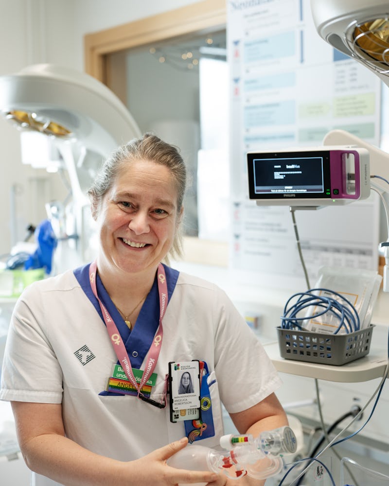 Angelica Robertsson står i ett medicinskt rum och håller i andningsutrustning. I bakgrunden syns monitorer och medicinteknisk utrustning.