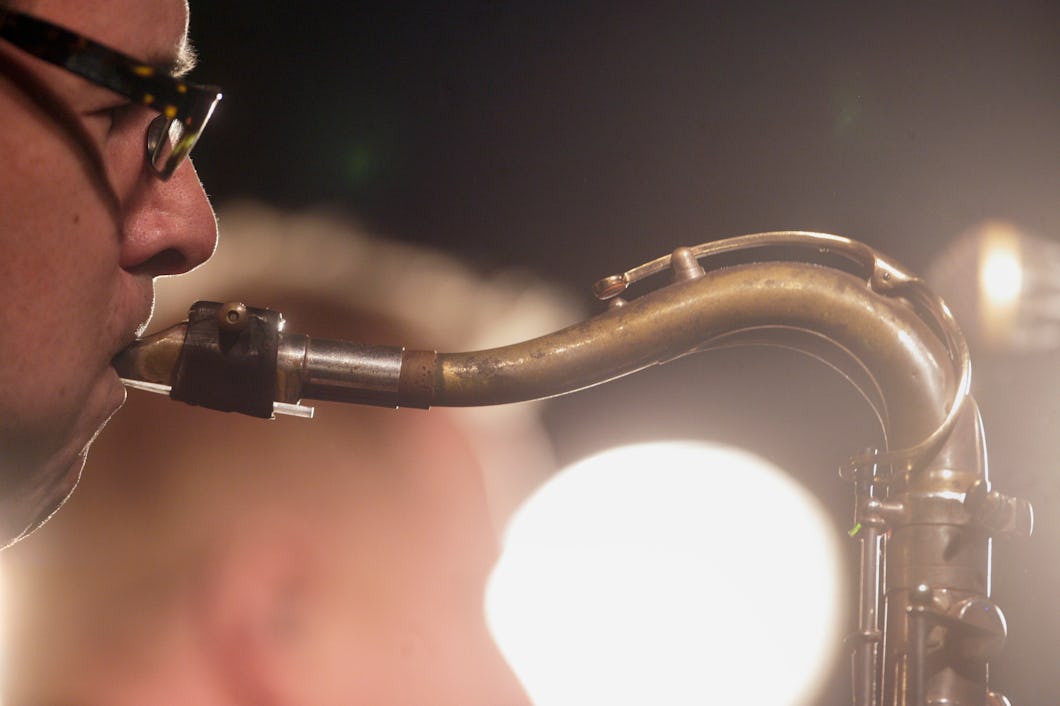 En sidobild på en person med glasögon som spelar saxofon. Ljussken syns i bakgrunden.