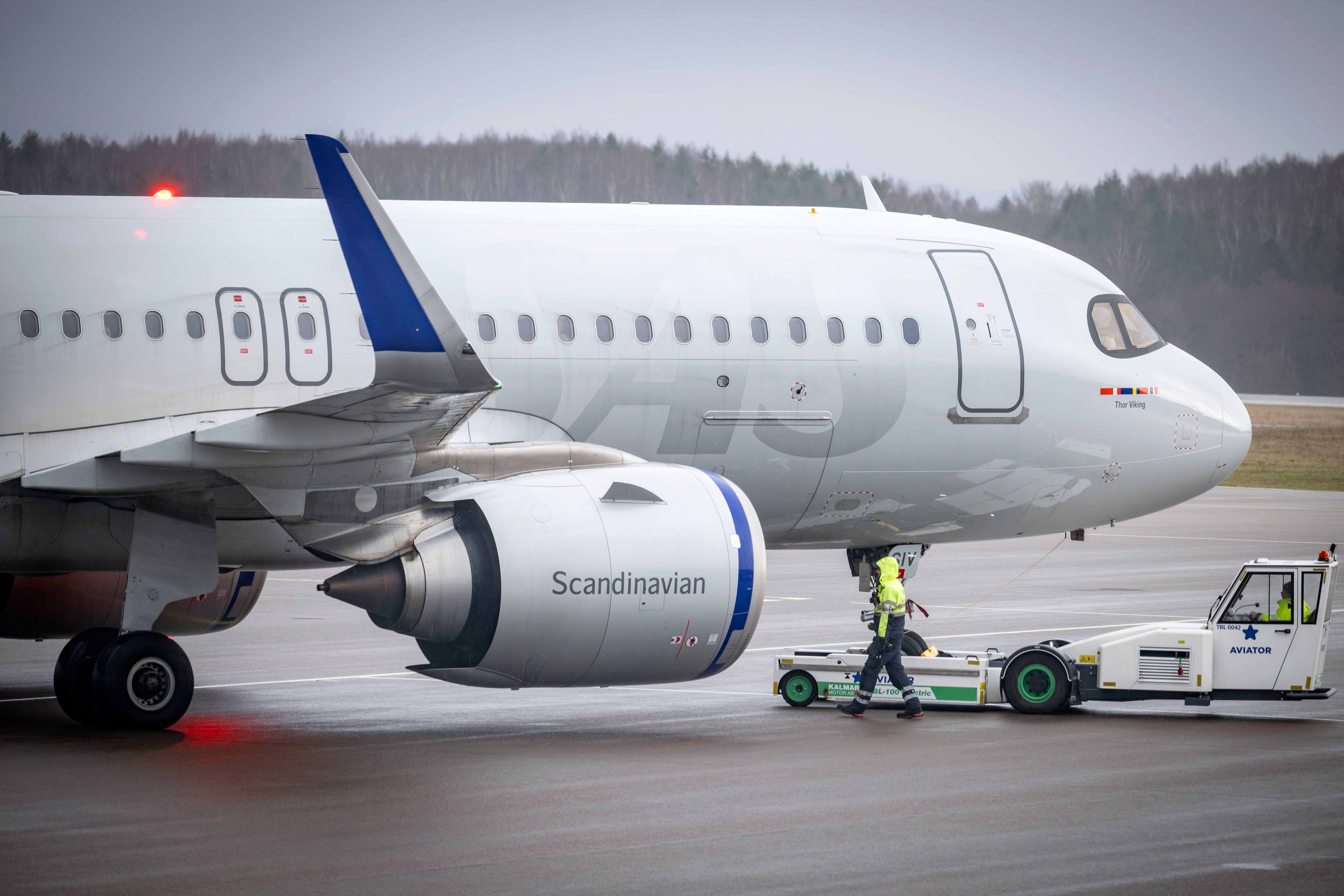 Ett flygplan från Scandinavian Airlines bogseras på en landningsbana av ett fordon. En arbetare i varseljacka går bredvid.