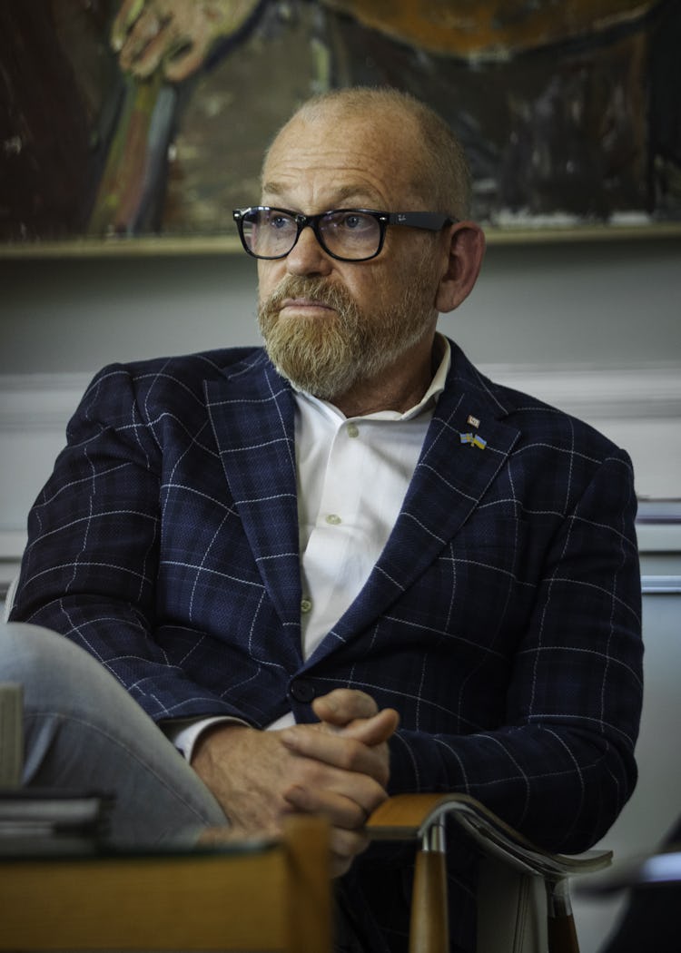 Johan Lindholm med glasögon och skägg sitter i en fåtölj. Han har händerna knäppta och bär en rutig jacka. Han tittar åt sidan.