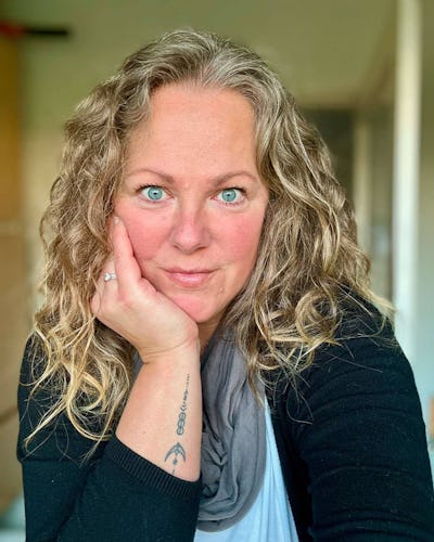 Malin Wallén med vågigt blont hår och blå ögon vill sitta ansikte mot handen och ser rakt in i kameran. Personen har på sig en svart tröja och en grå halsduk.