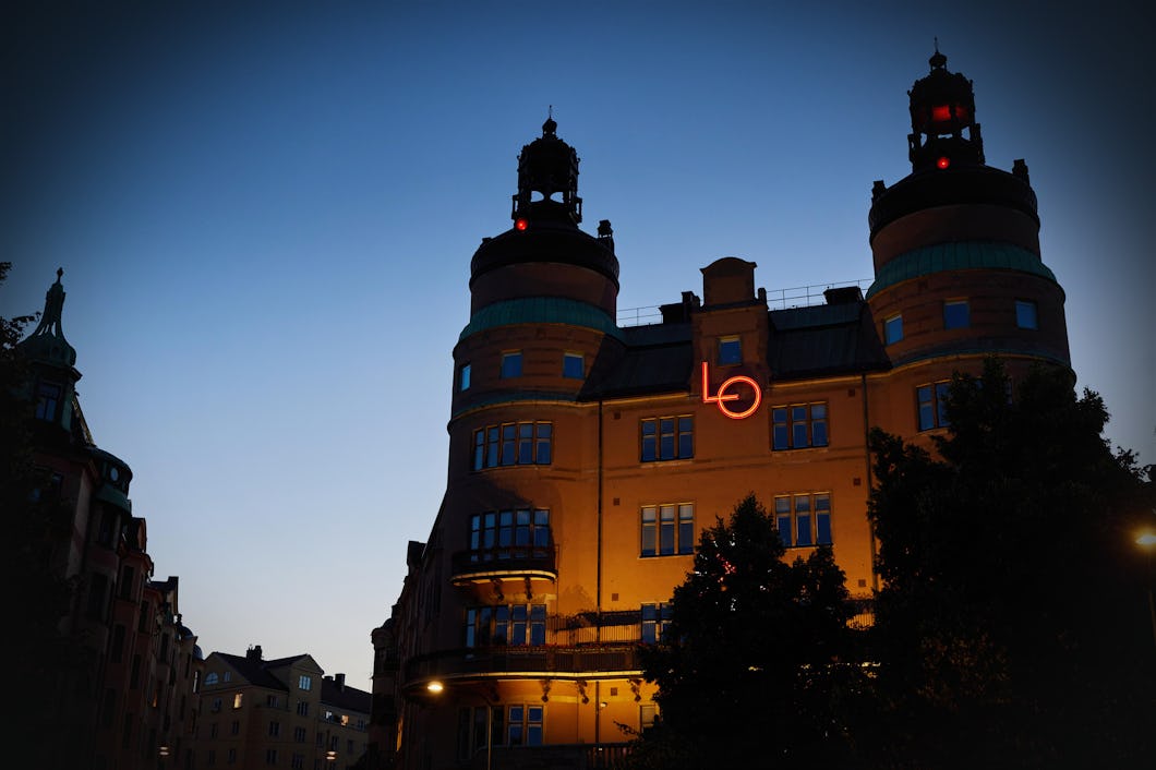 En byggnad med två runda torn är upplyst i skymningen. På fasaden sitter en röd neonskylt med texten "LO". Himlen är klar och det håller på att bli kväll.