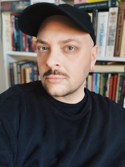 Edward Summanen med ljus hud, iklädd svart keps och svart tröja, står framför en bokhylla med böcker.