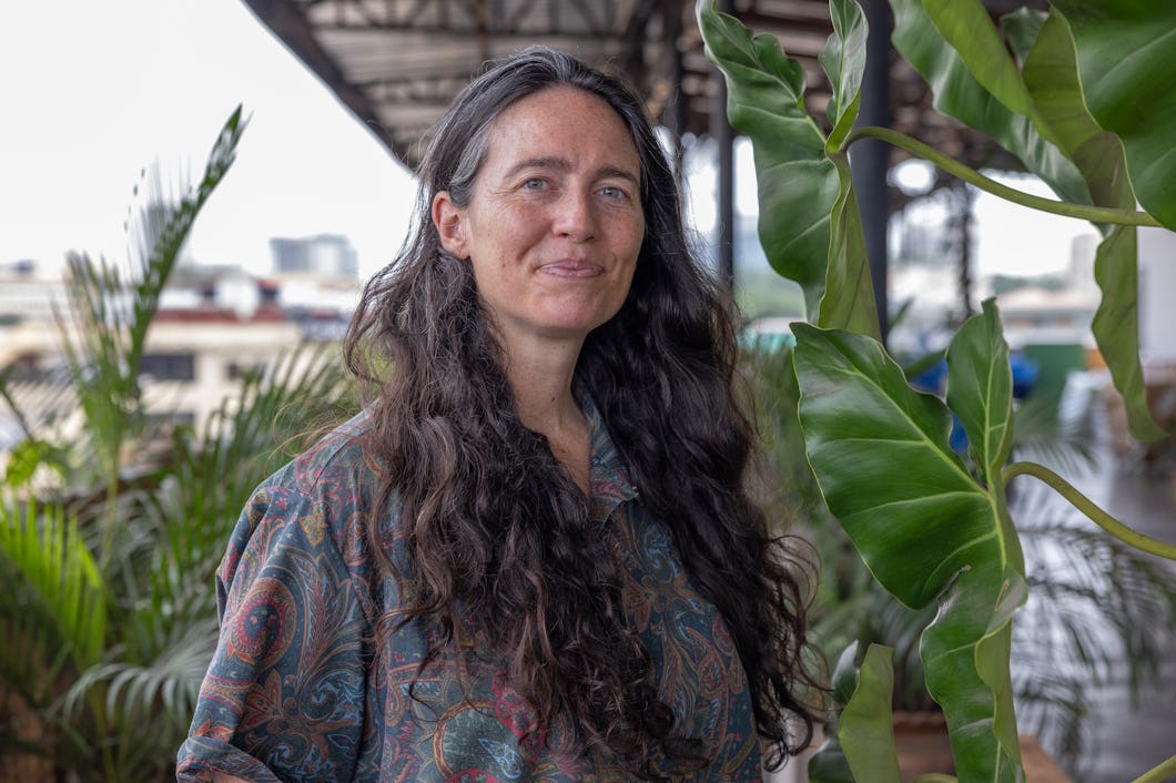 Liz Ricketts med gröna växter och byggnader i bakgrunden.