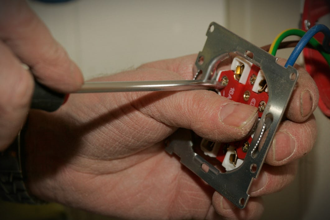 En person använder en skruvmejsel för att montera eller laga elektriska ledningar i ett vägguttag.
