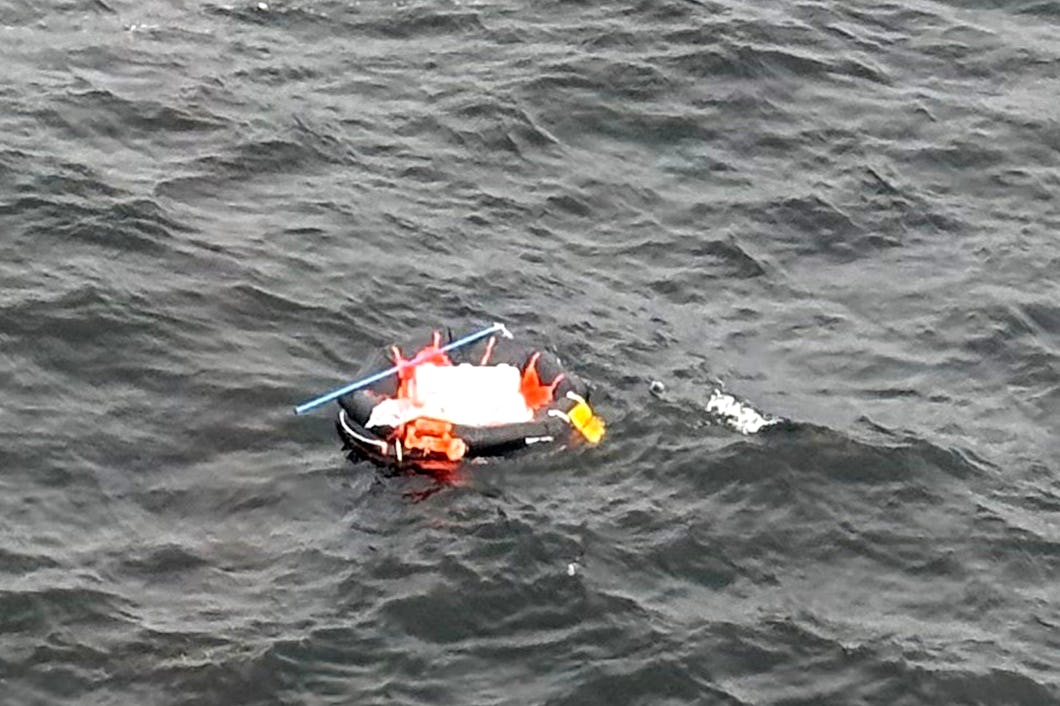 En uppblåsbar livbåt med personer i orange flytvästar driver på vattnet.