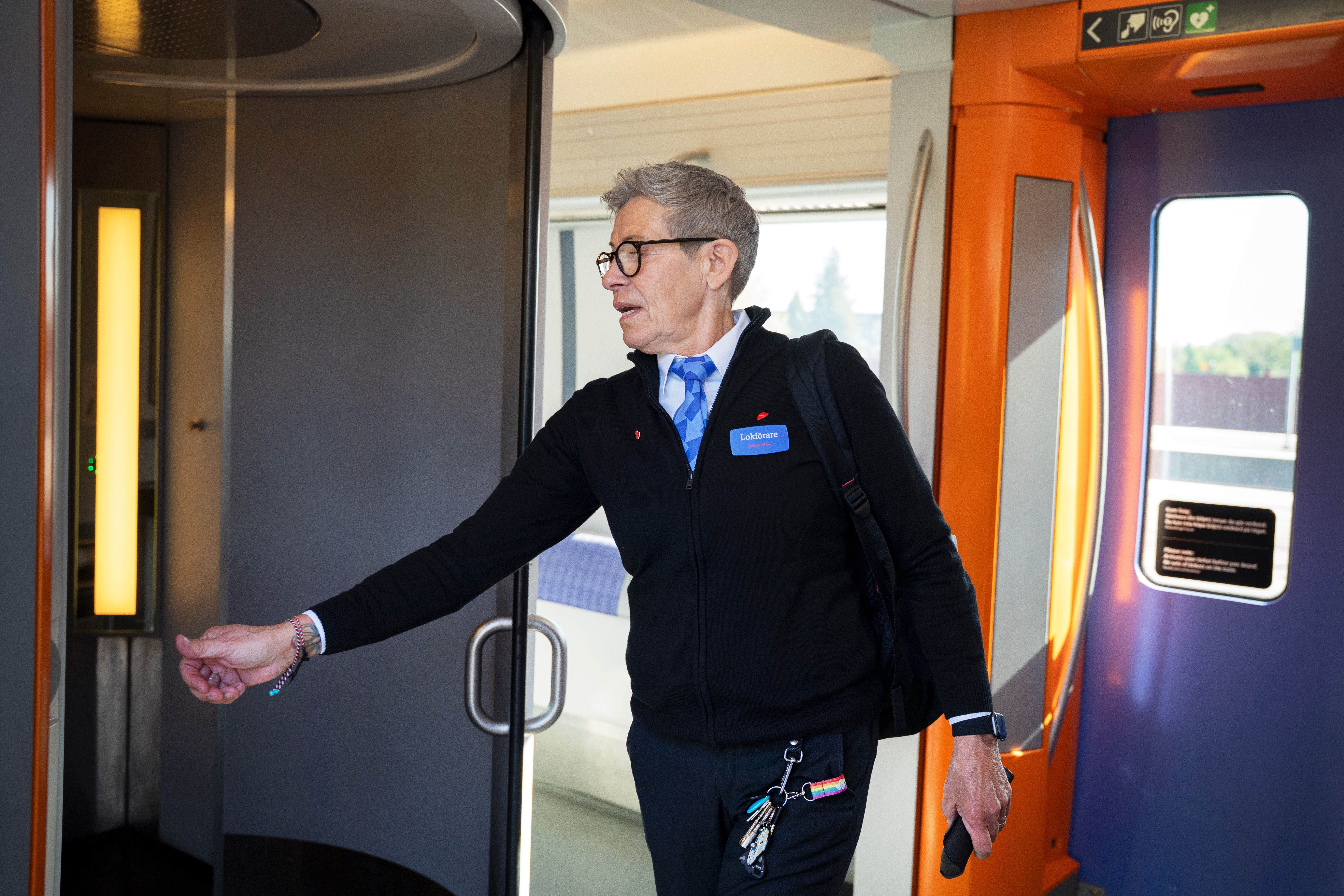 En äldre person i affärskläder med ett nyckelband och nycklar öppnar en dörr inne i ett tåg.