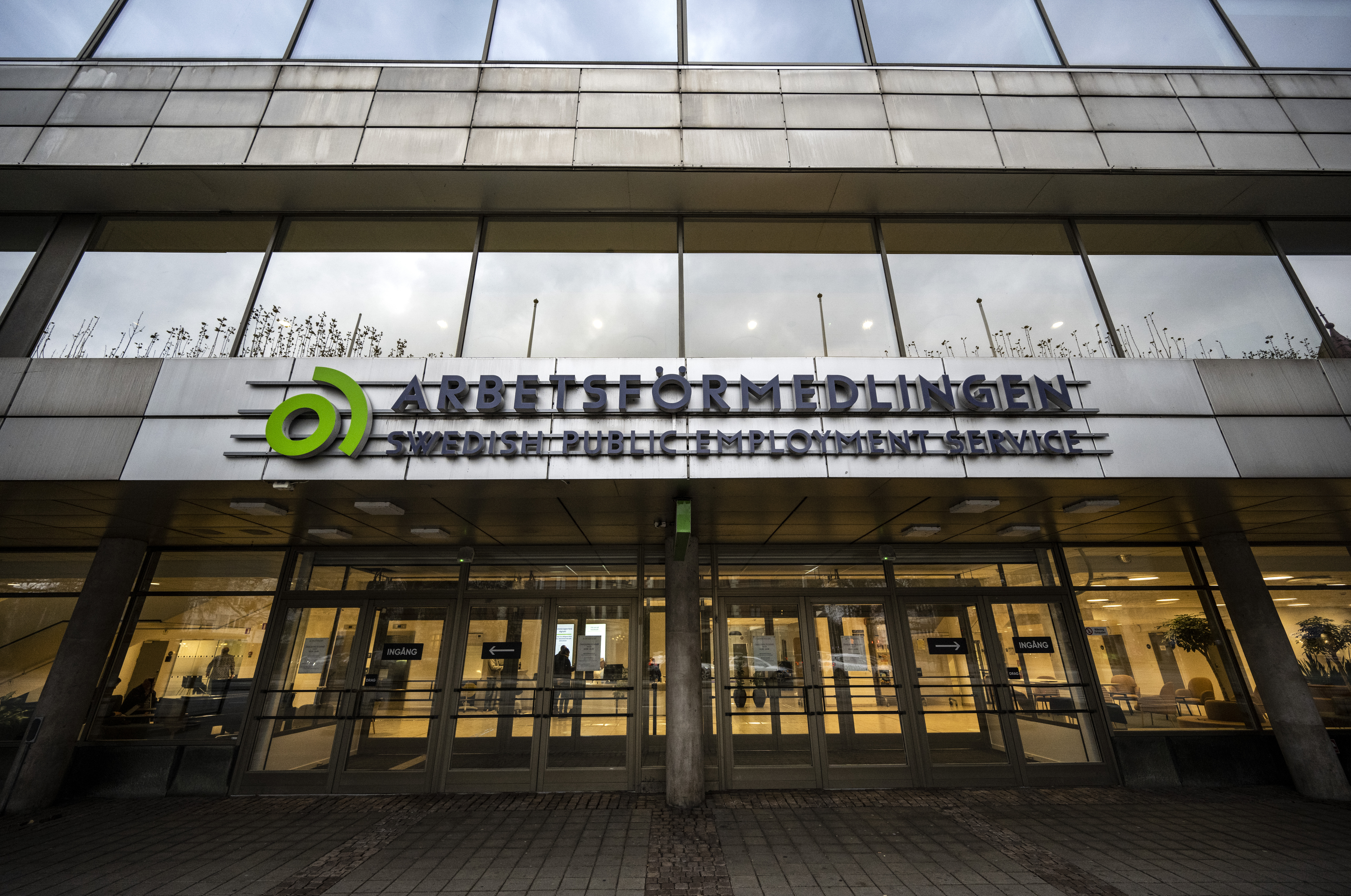 Entrén till Arbetsförmedlingen, Sveriges offentliga arbetsförmedling, med skyltar ovanför dörrarna och synliga lampor inomhus.