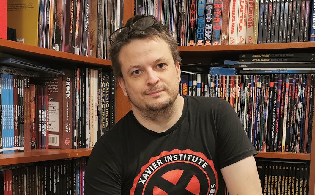 En person med en svart Xavier Institute-t-shirt sitter framför hyllor som är fyllda med grafiska romaner och serietidningar.