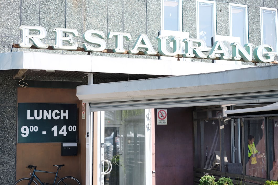 Utsidan av en restaurang med en skylt där det står "RESTAURANG" och en skylt med lunchens öppettider "9:00 - 14:00". En cykel står parkerad utanför.