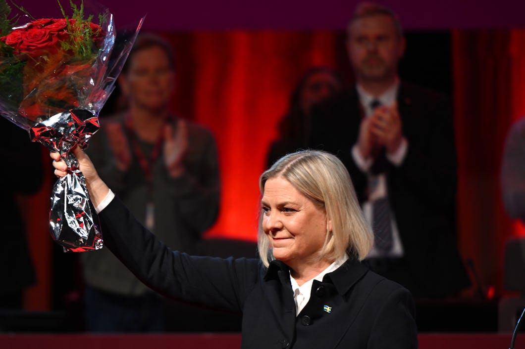 Magdalena Andersson i mörk kappa håller upp en bukett blommor på scenen, medan personer i bakgrunden applåderar.