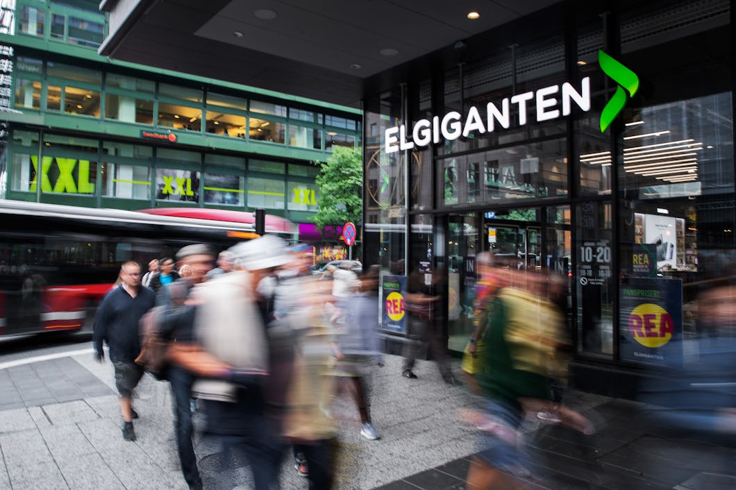 En grupp människor går framför en byggnad där det sitter en ”Elgiganten”-skylt.