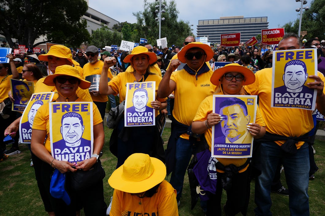En grupp personer i gula tröjor och hattar håller skyltar med texten "Free David Huerta" vid en utomhusprotest.