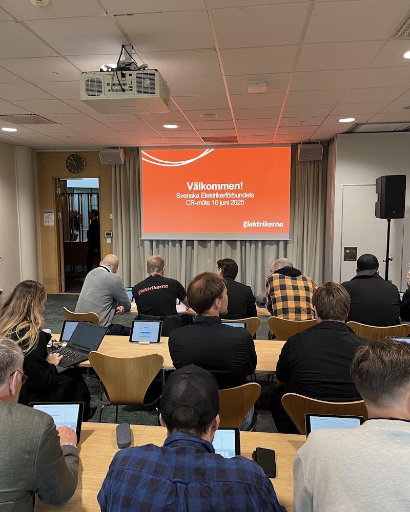 Personer sitter i ett konferensrum vända mot en skärm som visar ett välkomstmeddelande för Svenska Elektrikerförbundets årsmöte den 10 juni 2025.