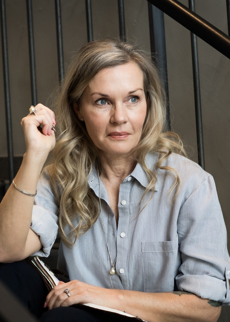 Pia Johansson med långt blont hår vid en trappa. Hon håller i ett anteckningsblock och en penna och tittar åt sidan.