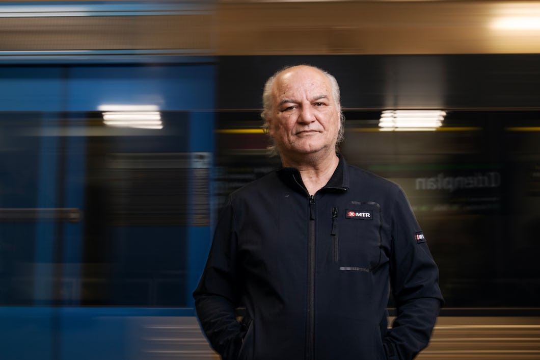 En äldre man i jacka står framför ett tåg och tittar rakt in i kameran med neutral min.