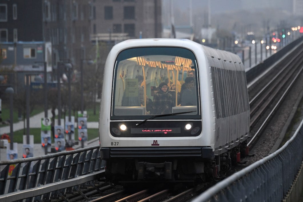 Ett tunnelbanetåg åker på upphöjda spår genom ett stadsområde, och passagerare syns genom det främre fönstret.