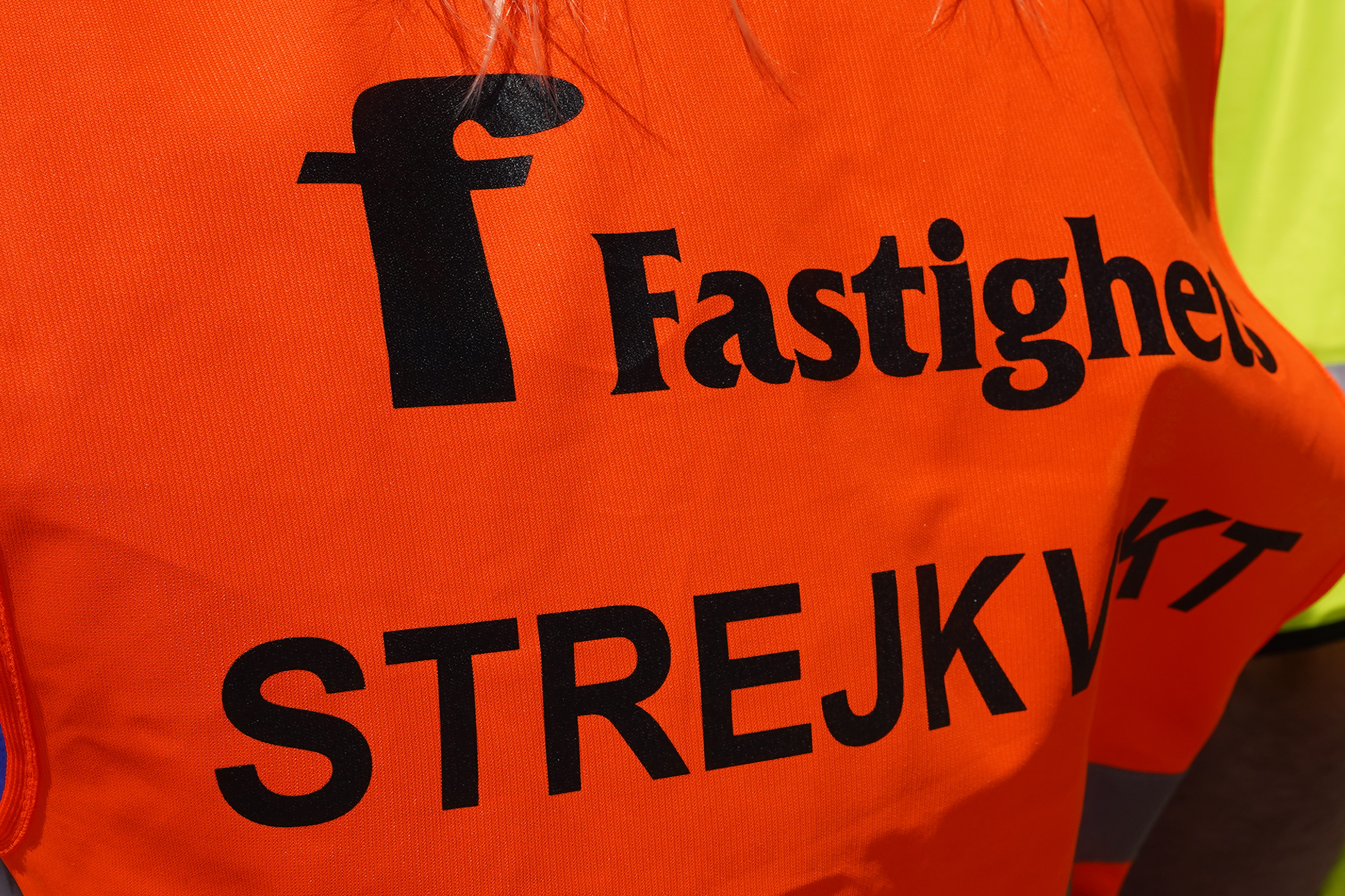 En person har på sig en väst med orden "Fastighets" och "STREJKVAKT" tryckta i svart text.