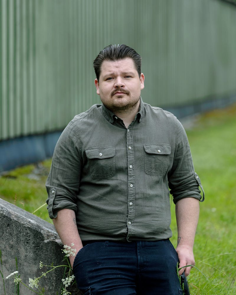 Lennie Eriksson med mörkt hår och kort skägg står utomhus bredvid ett betonggräcke och en vägg av korrugerad plåt.