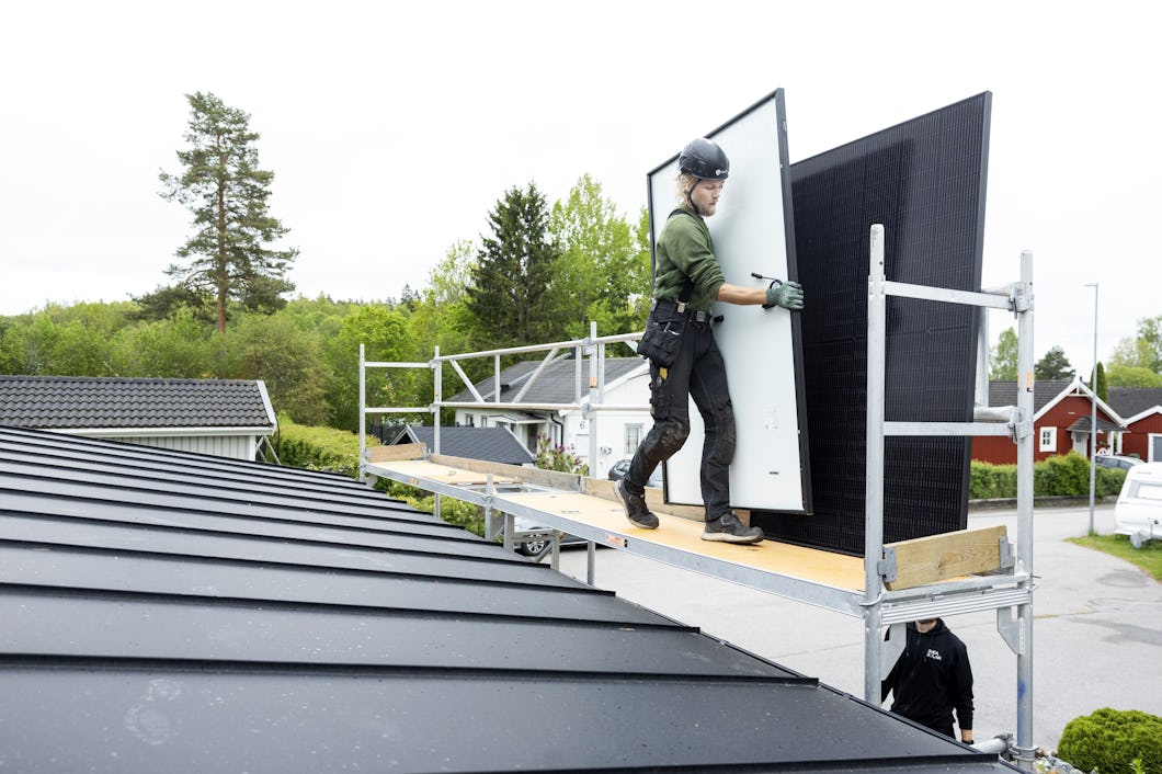En arbetare med skyddsutrustning monterar en solpanel på en takställning i ett bostadsområde.