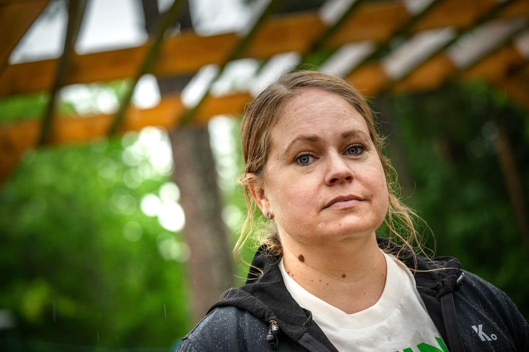 En kvinna med ljust brunt hår och blå ögon står utomhus under en träkonstruktion. Hon har på sig en svart jacka och en vit skjorta och visar ingen tydlig min.