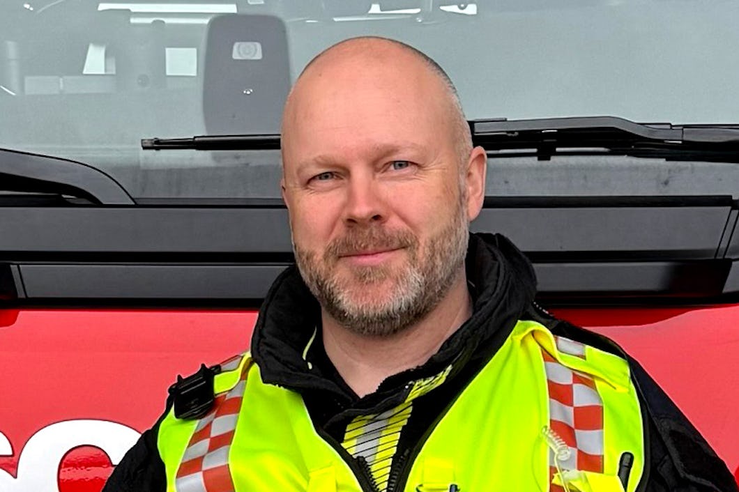 Brandmannen Christian Åås. med en gul reflexväst står framför en brandbil.