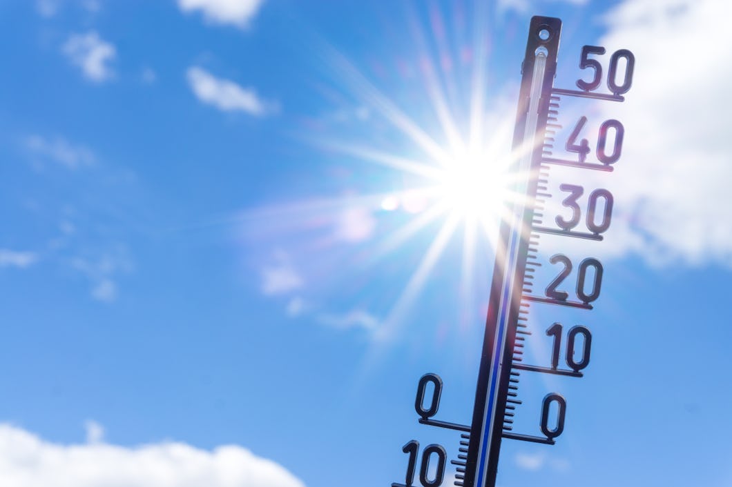 En termometer som visar temperaturer upp till 50°C är placerad utomhus under en himmel med sol och några moln.