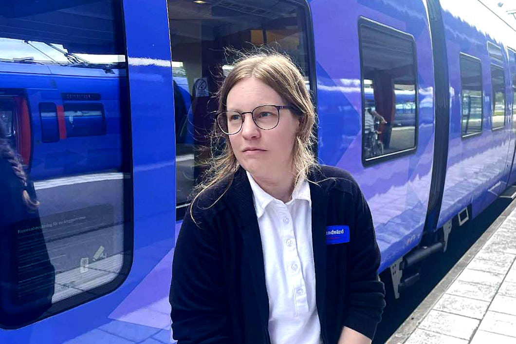 Tågvärden Samantha Nordahl med glasögon och jacka står på en tågperrong bredvid ett blått tåg.