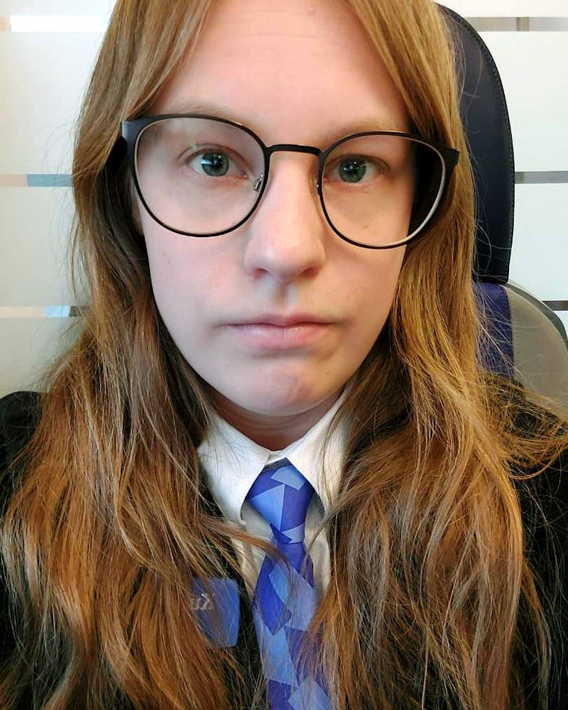 Tågvärden Samantha Nordahl med långt ljust brunt hår och glasögon har på sig kostym och blåmönstrad slips, sitter inomhus och är vänd mot kameran.