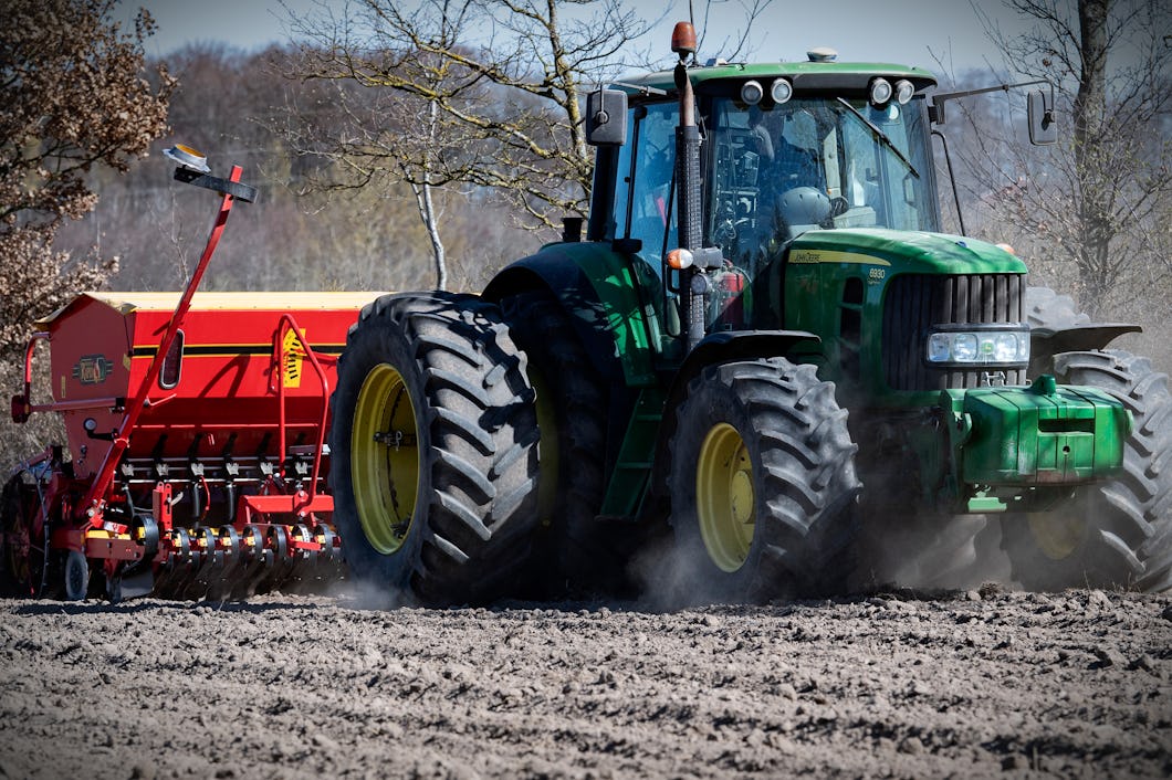 En traktor drar en såmaskin över en plöjd åker för att göra marken redo för sådd under dagen.