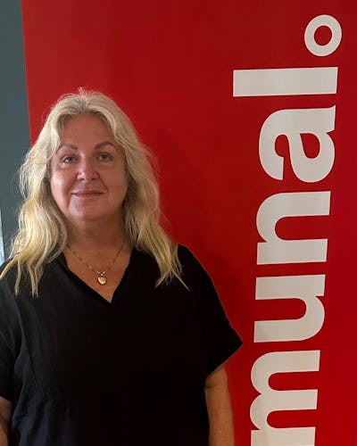 Beata Nilsson med långt blont hår står framför en röd, vertikal skylt med vit text där det står Kommunal. Hon har på sig en svart topp och ett halsband.