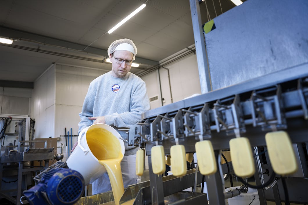 En arbetare i en fabrik häller en vätskeblandning från en behållare i en maskin som fyller formar och tillverkar stavar.