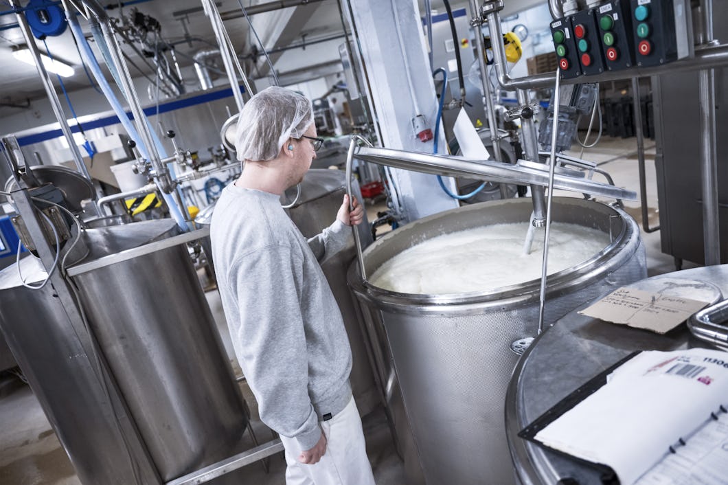 En person i skyddskläder övervakar en stor tank av rostfritt stål med vätska i en livsmedelsanläggning.