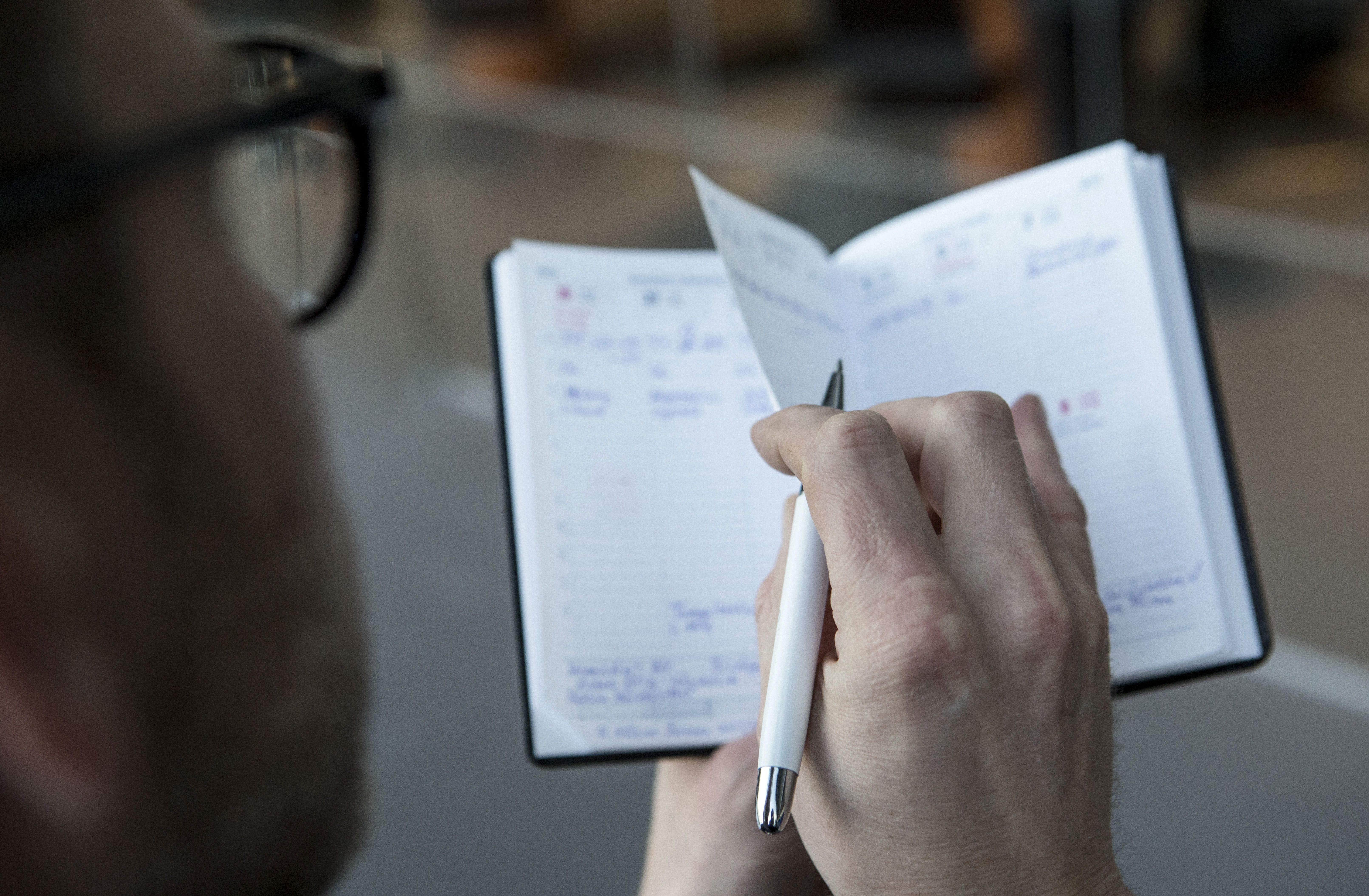 En person bläddrar i en öppen kalender med anteckningar och bokade tider, medan de håller i en penna.