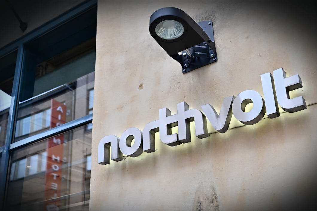 Byggnadens utsida har en upplyst skylt med texten "northvolt" som sitter på en beige vägg, bredvid ett fönster och under en utomhuslampa.
