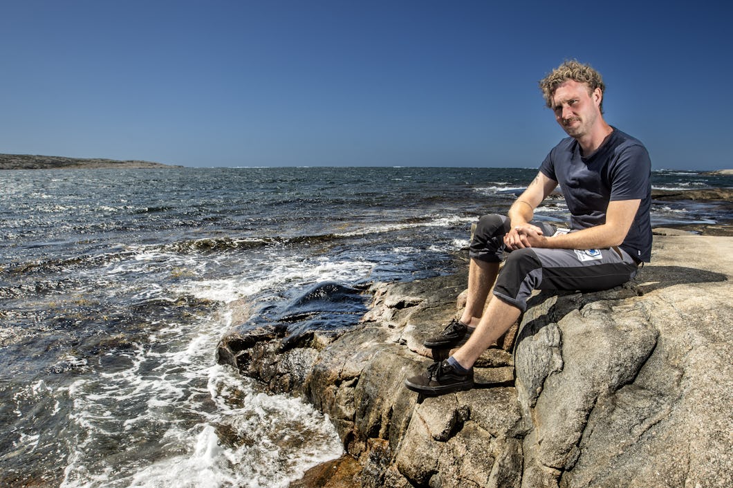 Brian Mortensen sitter på klippor vid havet under en klar himmel en solig dag.