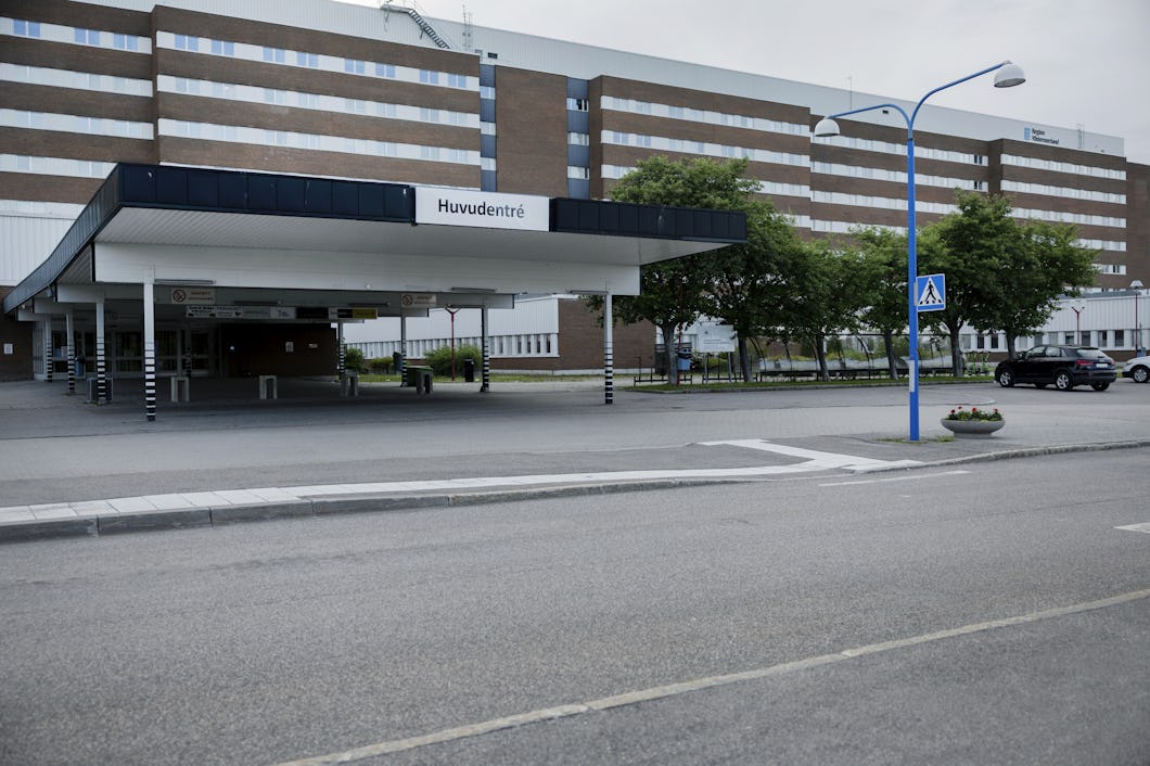 Ett sjukhus med huvudentré-skylt på svenska, några träd och en parkeringsplats framför.