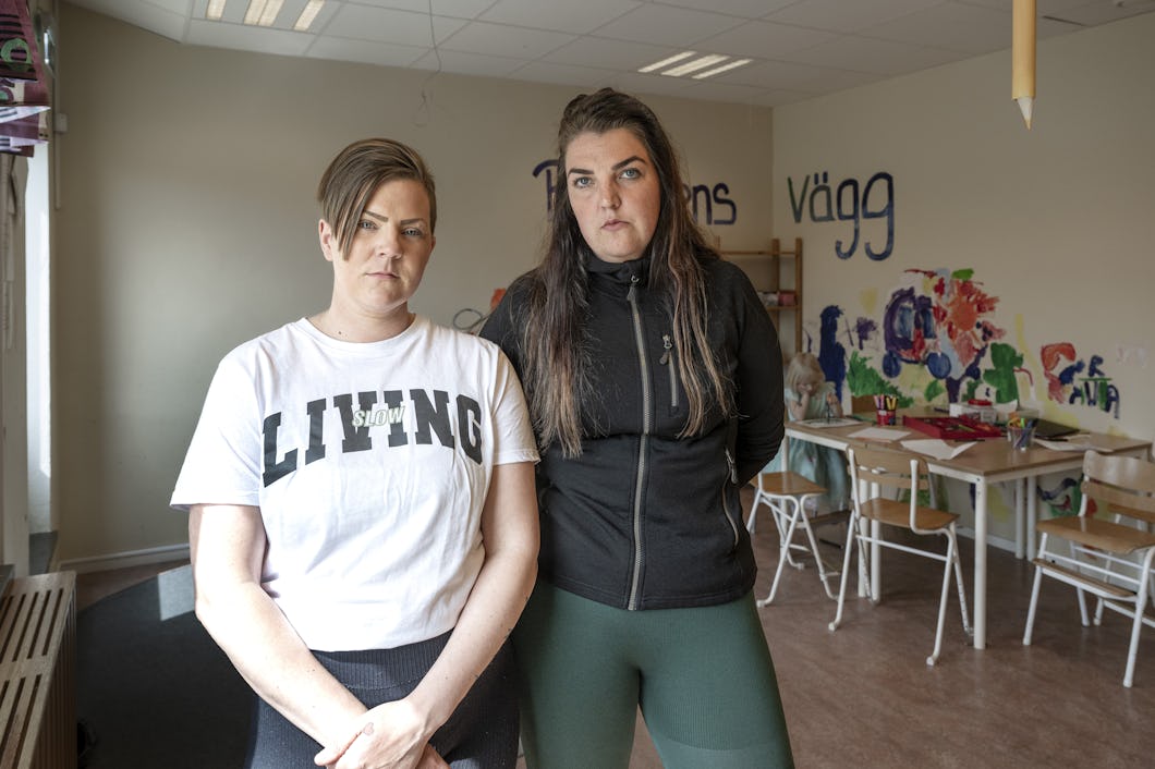 Två kvinnor står bredvid varandra i ett klassrum. På väggarna sitter barns teckningar. I bakgrunden finns bord och stolar.