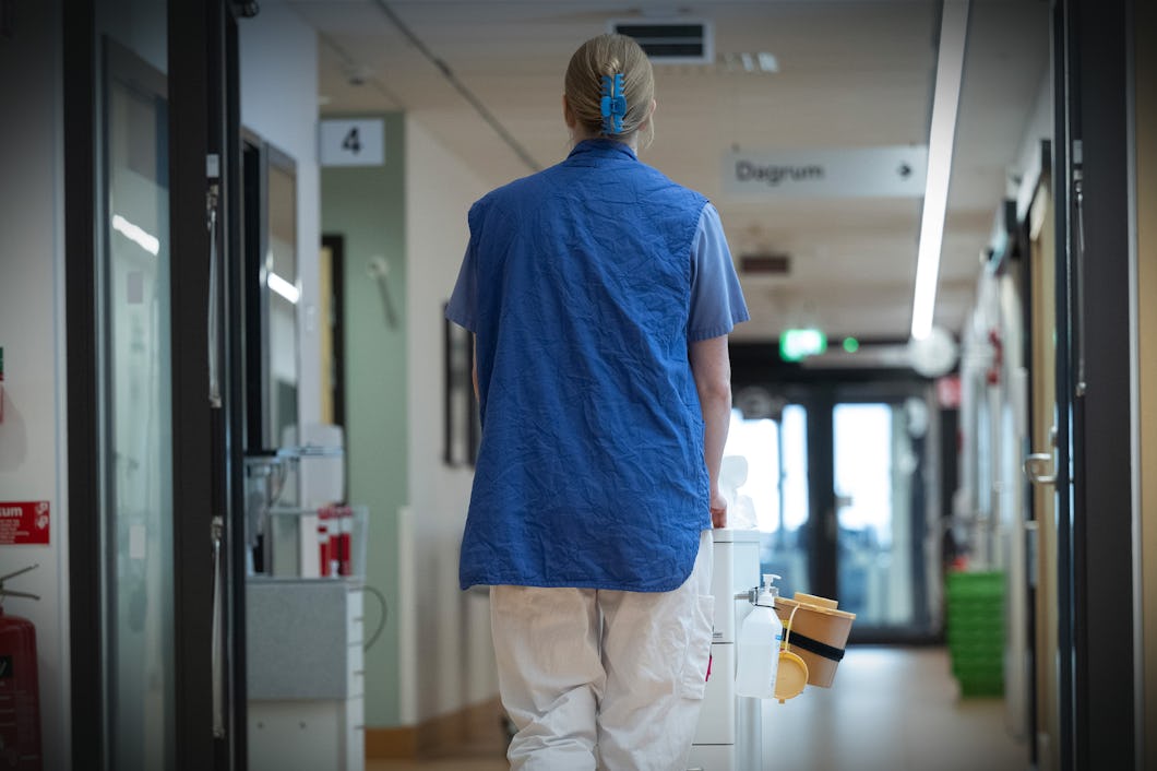 En person i medicinska kläder går i en sjukhuskorridor och skjuter på en vagn.