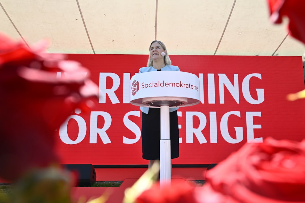 Socialdemokraternas partiledare Magdalena Andersson står vid ett podium med Socialdemokraternas logotyp och talar på en utomhusscen. Framför henne finns rosor och bakom henne finns en stor röd skylt.